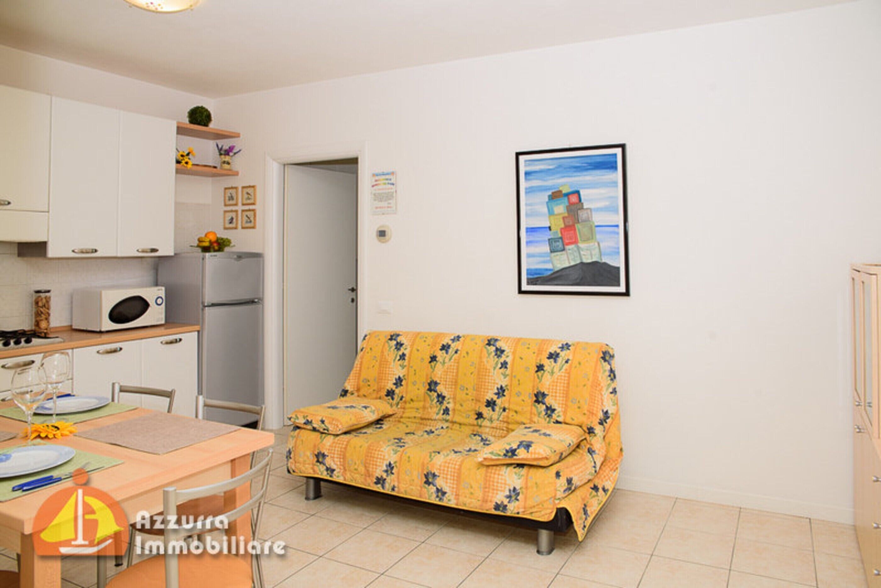 Un espacio habitable compacto con kitchenette, un sofá, una mesa de comedor y un cuadro en la pared.