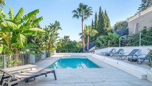 A swimming pool with lounge chairs, surrounded by tropical plants and a clear sky. - Villa 'Jazmin' with Mountain View, Wi-Fi and Air Conditioning (Mijas Costa)
