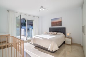 Un dormitorio con cama, mesita de noche, lámpara, ventana con cortinas y vistas al exterior.