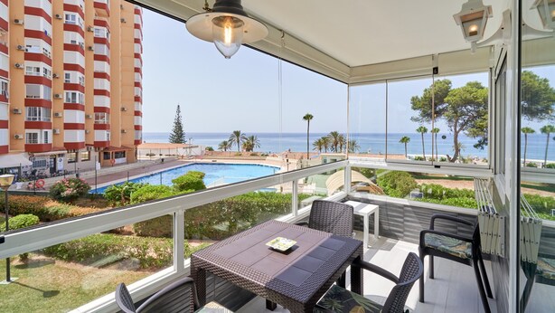 A balcony with a table and chairs, overlooking a swimming pool and a building with balconies. - Apartment 'Primera Línea con Terrace A104' with Sea View, Shared Pool and Wi-Fi (Torrox)