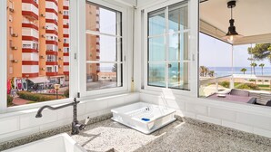 A modern bathroom with a granite countertop, a white sink, a window with a view of a building and the sea, and a hanging light fixture. - Apartment 'Primera Línea con Terrace A104' with Sea View, Shared Pool and Wi-Fi (Torrox)