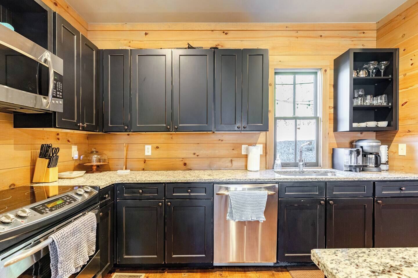 A modern kitchen with dark cabinets, a stainless steel stove, and a coffee maker.