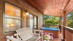 A wooden deck with a hot tub, a wooden Adirondack chair, and a table with a vase of flowers.