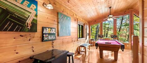 A wooden cabin interior with a pool table, bar area, and artwork on the walls.