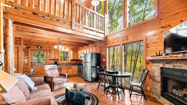 A cozy cabin interior with a living room, dining area, kitchen, and a fireplace.