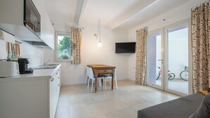 A compact kitchen with a dining area, a TV mounted on the wall, and a sliding glass door leading to an outdoor area. - Apartment "Casa Mavi" with Shared Terrace, Wi-Fi & Air Conditioning (Corte Franca)