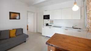 A modern kitchen with white cabinets, a built-in microwave, and a sink. There's a wooden dining table and a gray sofa with a yellow pillow. - Apartment "Casa Mavi" with Shared Terrace, Wi-Fi & Air Conditioning (Corte Franca)