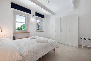 Une chambre à coucher avec un lit, deux fenêtres, une armoire et un banc.