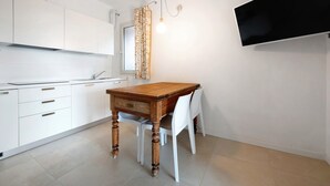A modern kitchen with white cabinetry, a wooden dining table, and a flat-screen TV mounted on the wall. - Apartment "Casa Mavi" with Shared Terrace, Wi-Fi & Air Conditioning (Corte Franca)