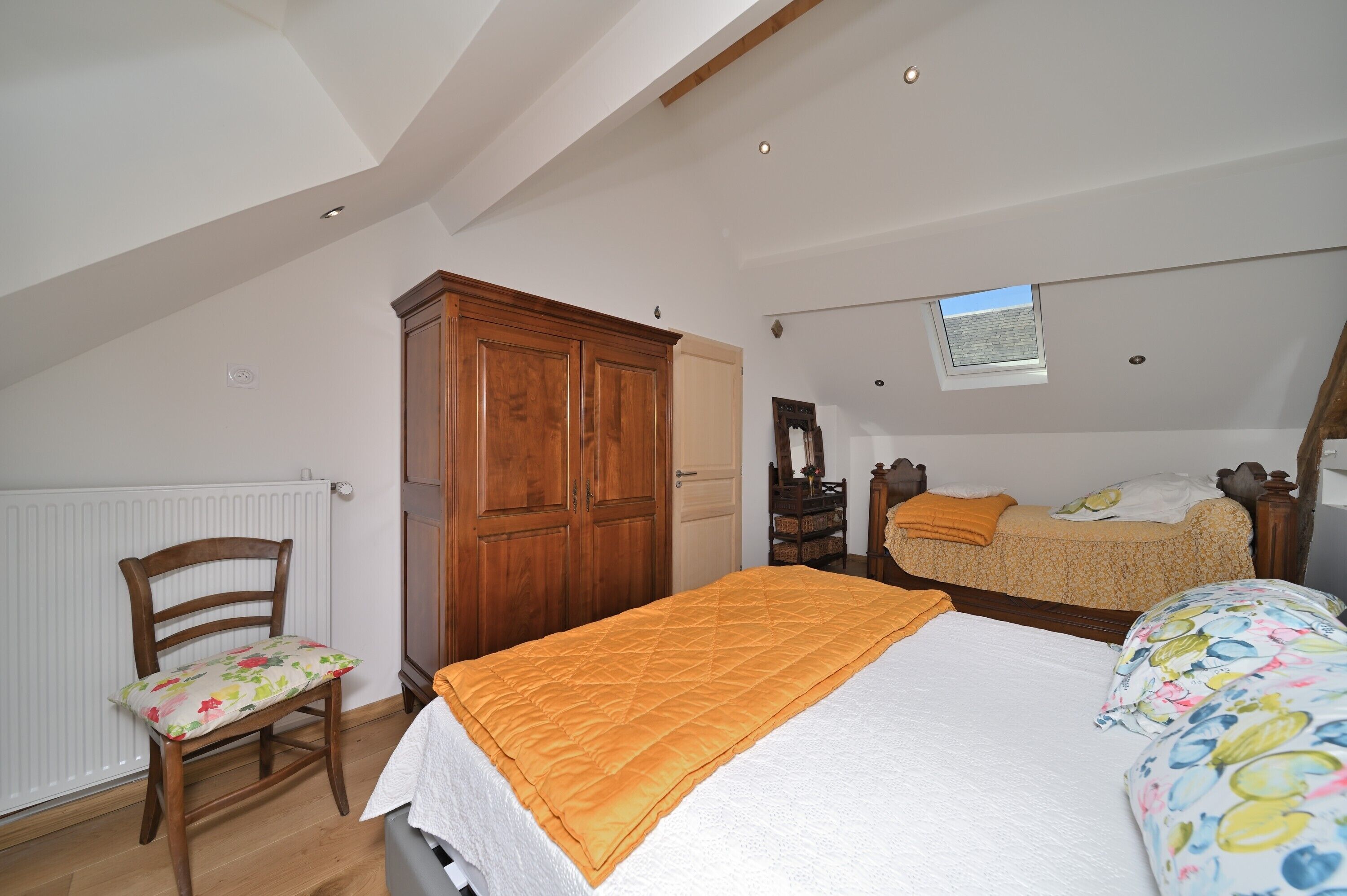 Un dormitorio con cama, armario de madera, una silla, radiador y ventana.