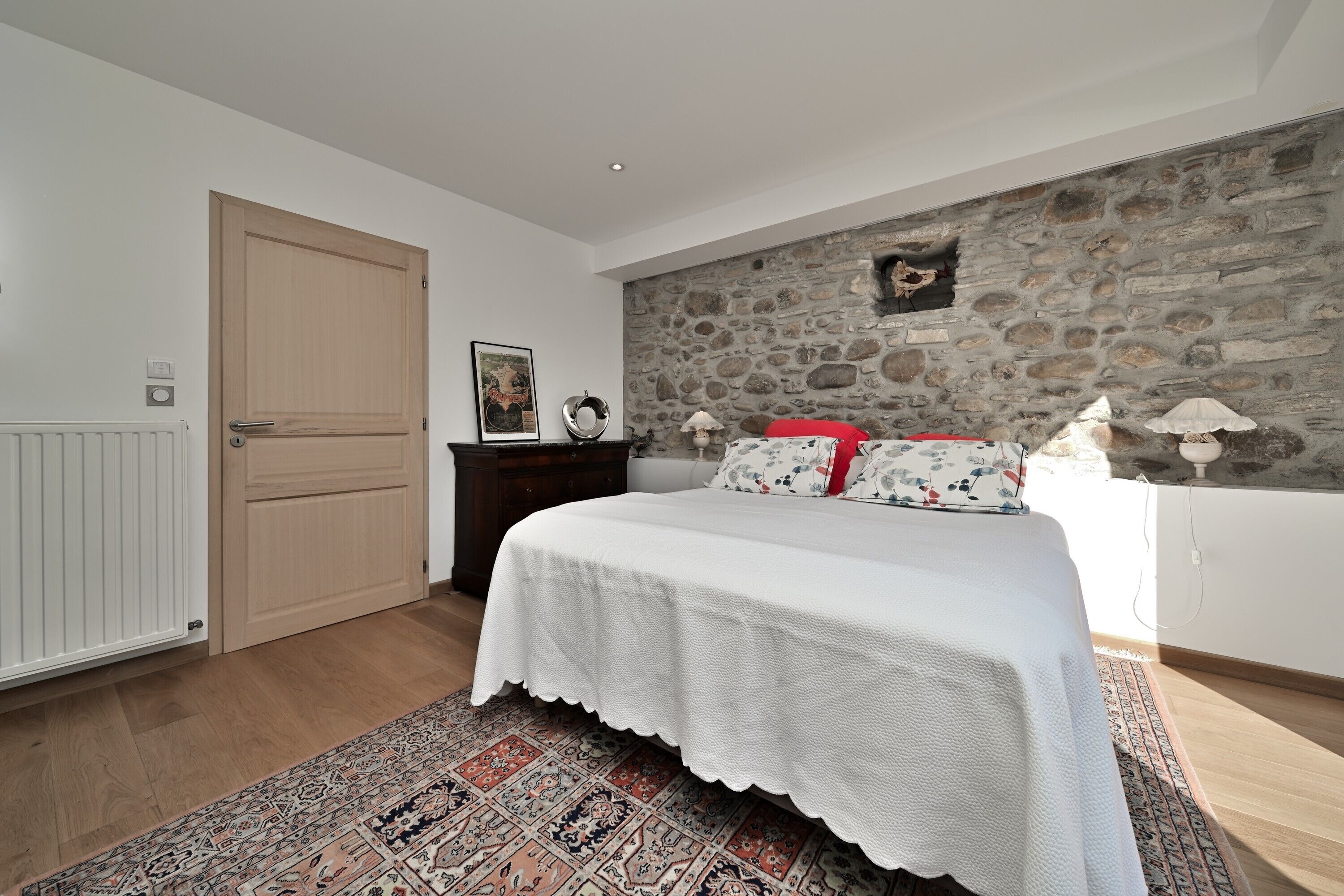 Ein Schlafzimmer mit einem Bett, einer Steinwand, einer Holztür und einer Heizung.