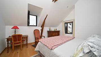 Un dormitorio con cama, escritorio, silla, ventana y una viga de techo de madera.