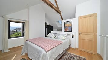 Een slaapkamer met een bed, dakraam, houten deur en uitzicht op bergen.