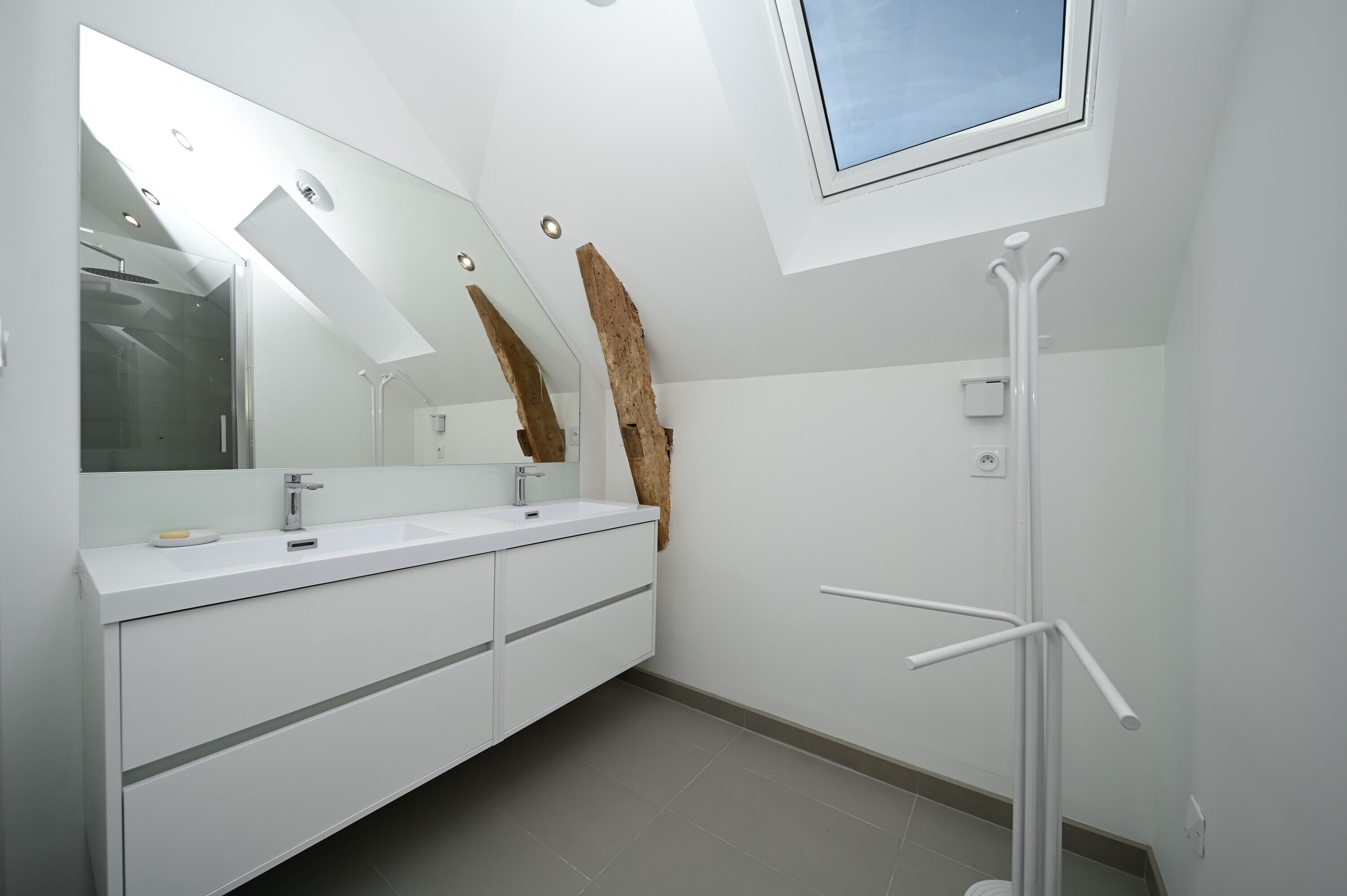 A modern bathroom with a skylight, a large mirror, and a white vanity.