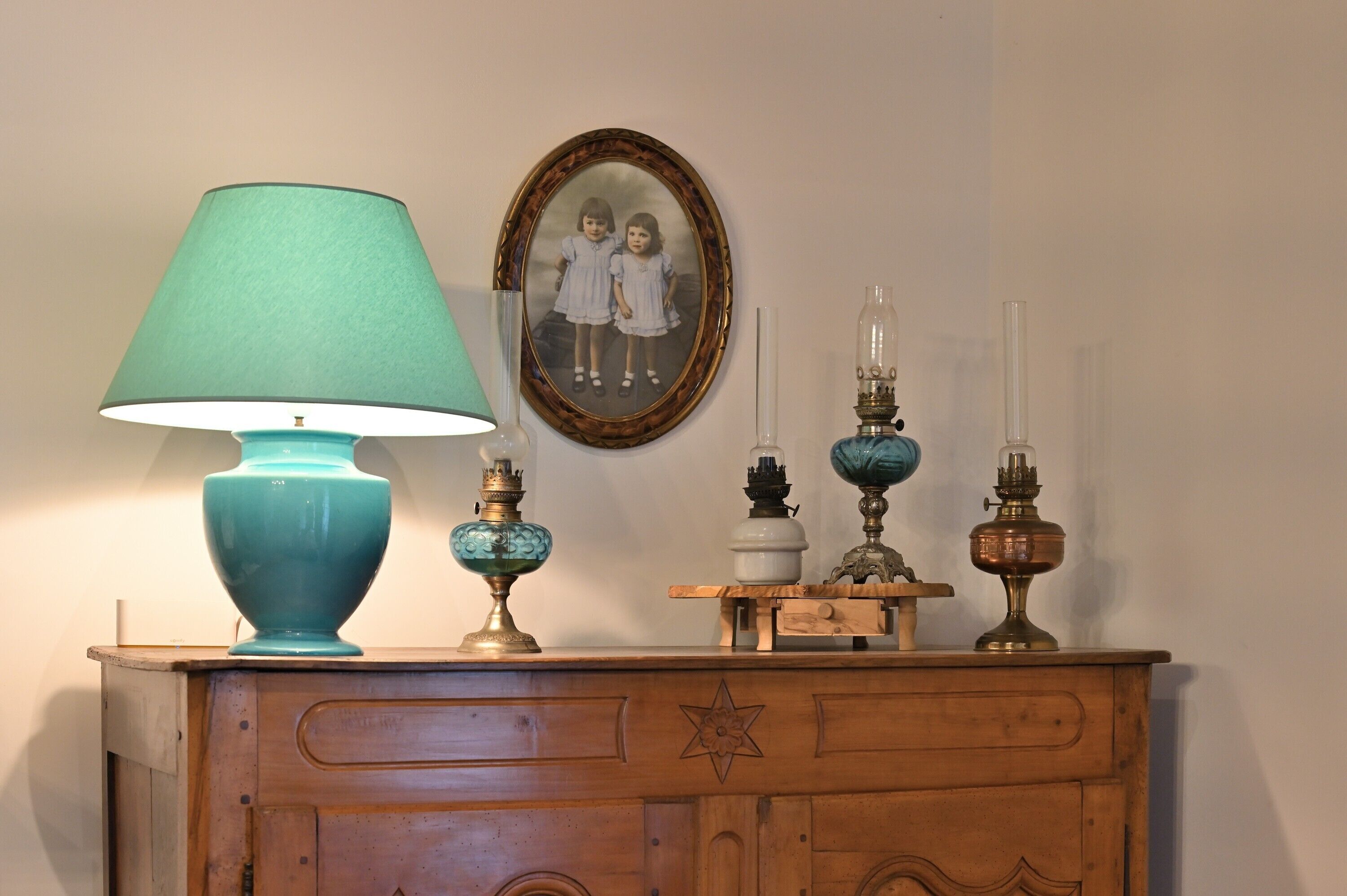 Et trækommode med en teal-farvet lampe, et indrammet fotografi og flere dekorative genstande.
