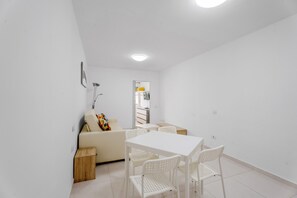 Una stanza piccola con pareti bianche, un tavolo e sedie bianchi, un divano beige e un tavolino in legno.