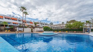 A swimming pool with a small island in the center, surrounded by a stone wall and palm trees. - Vacation Apartment 'Costa Del Silencio Tenerife Sur' with Shared Pool and Wi-Fi (Arona)