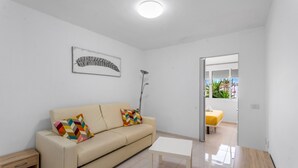A modern living room with a beige sofa, a colorful geometric pillow, a white coffee table, a floor lamp, and a framed artwork on the wall. - Vacation Apartment 'Costa Del Silencio Tenerife Sur' with Shared Pool and Wi-Fi (Arona)