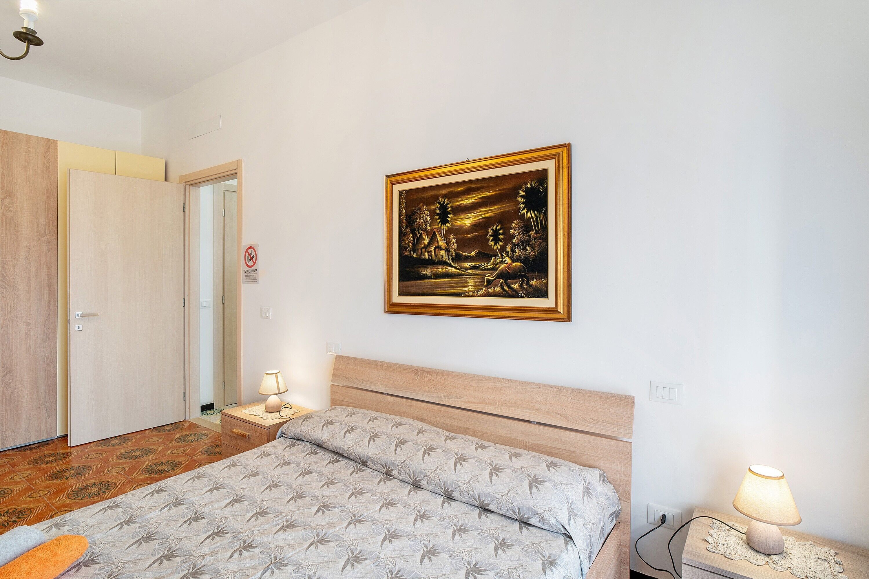 Quarto com cama, abajures, mesa de cabeceira, quadro emoldurado e porta.