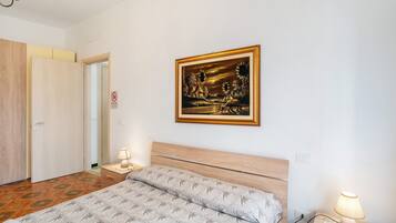 Quarto com cama, abajures, mesa de cabeceira, quadro emoldurado e porta.