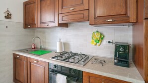 Una cocina con armarios de madera, un lavamanos de acero inoxidable, una estufa a gas y una cafetera.