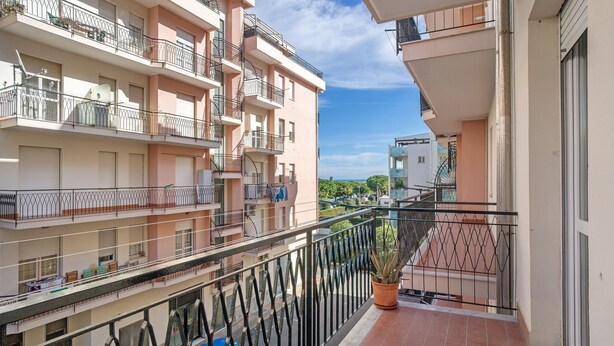 Un edificio residencial de varios pisos con balcones, una planta en maceta y un cielo despejado.