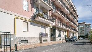 Un edificio residencial de varios pisos con balcones, entrada protegida y automóviles estacionados.