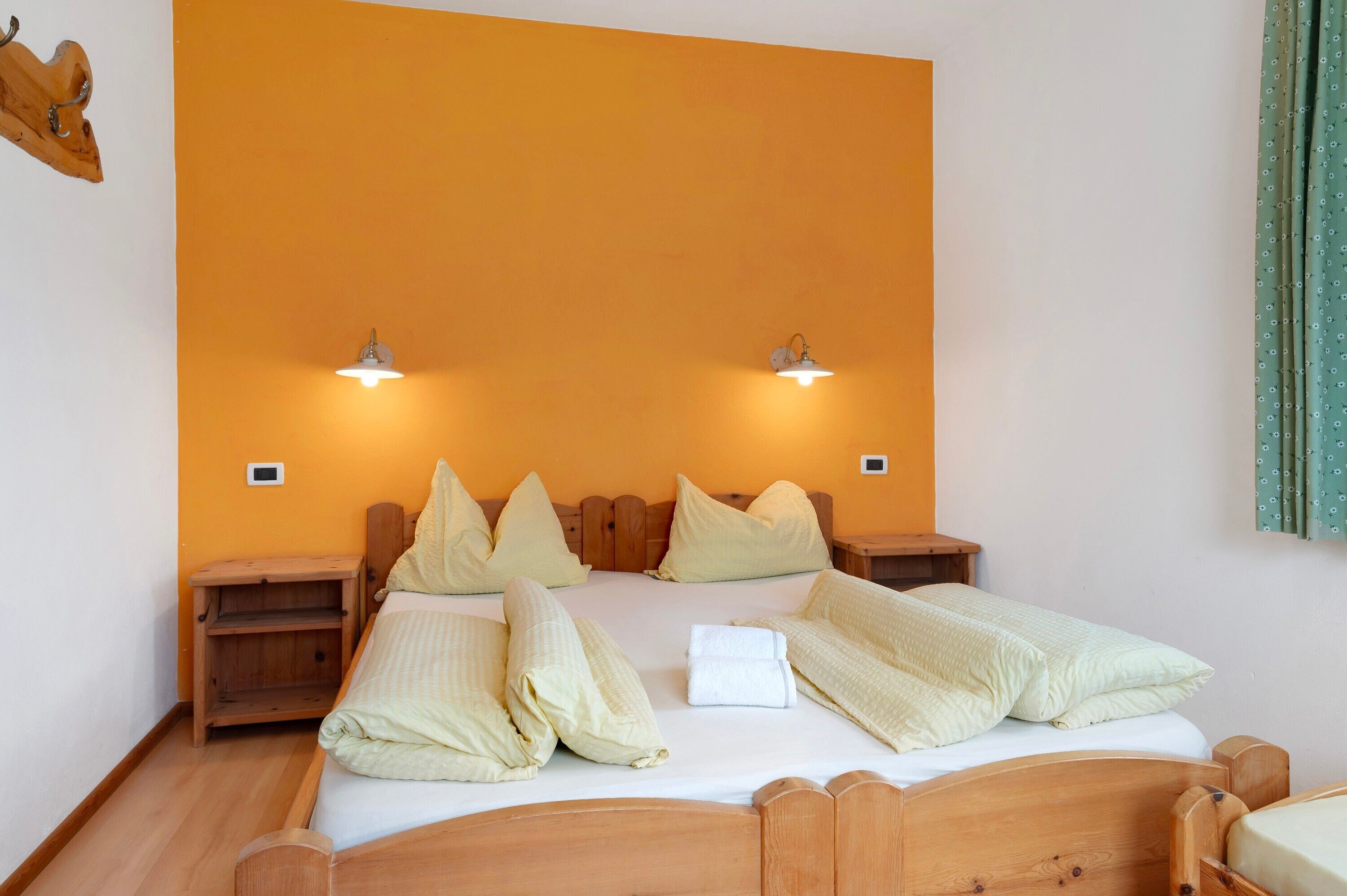 Un lit double avec une tête de lit en bois, deux tables de chevet et deux lampes fixées au mur.