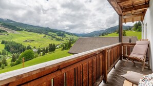 Un balcon en bois offrant une vue sur des collines verdoyantes et un ciel nuageux.