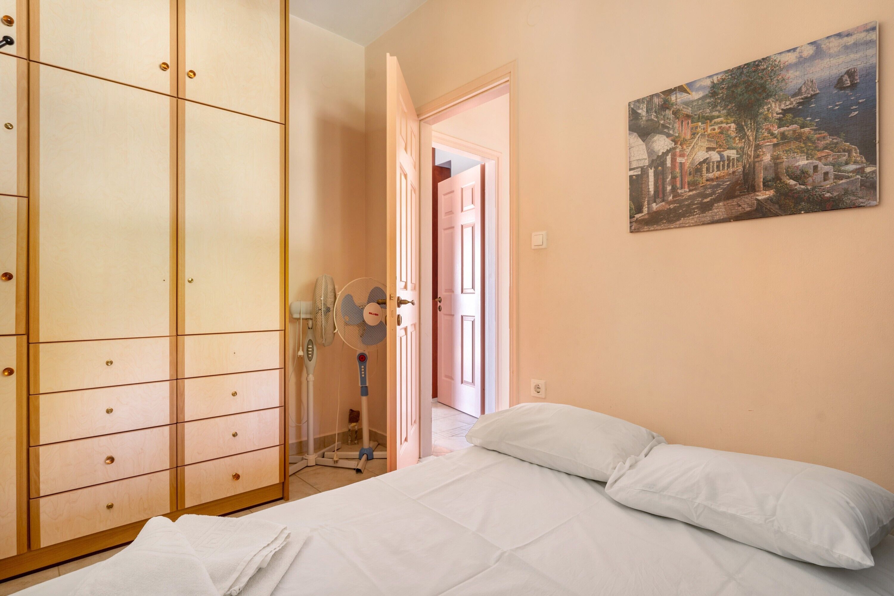 Une chambre à coucher avec un lit, une armoire, un tableau et une porte donnant sur une autre pièce.