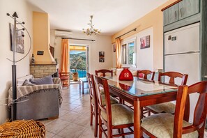 Un espace repas avec une table en verre et des chaises en bois, un canapé, une cheminée et une vue sur l’extérieur.