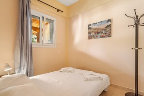 Une chambre d’hôtel avec un lit, une fenêtre avec des rideaux, un porte-manteau et un tableau au mur.