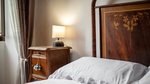 Een net opgemaakt bed met witte lakens, een houten nachtkastje met een lamp, en een houten hoofdbord met bloemversieringen.