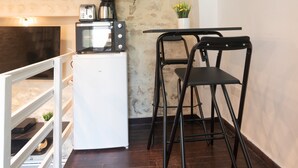 A compact kitchen with a built-in microwave, a coffee maker, and a small refrigerator. There are two black chairs and a small table. A large wall clock is mounted above the counter. - Apartment 'Duplex Parisien Charmant Métro13' with Wi-Fi (Paris)