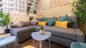 A modern living room with a grey sofa, teal and yellow cushions, a small round table, and a potted plant. - Apartment 'Duplex Parisien Charmant Métro13' with Wi-Fi (Paris)