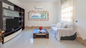A living room with a flat-screen TV, a coffee table with a vase, a sofa, a bookshelf, and a window with a view. - Villa with Jacuzzi & Fitness Area – Private Spaces & Exclusive Areas – Arenella Mare (Arenella)
