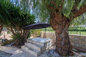 A hot tub with stone steps, a tree, and an umbrella in a garden setting.