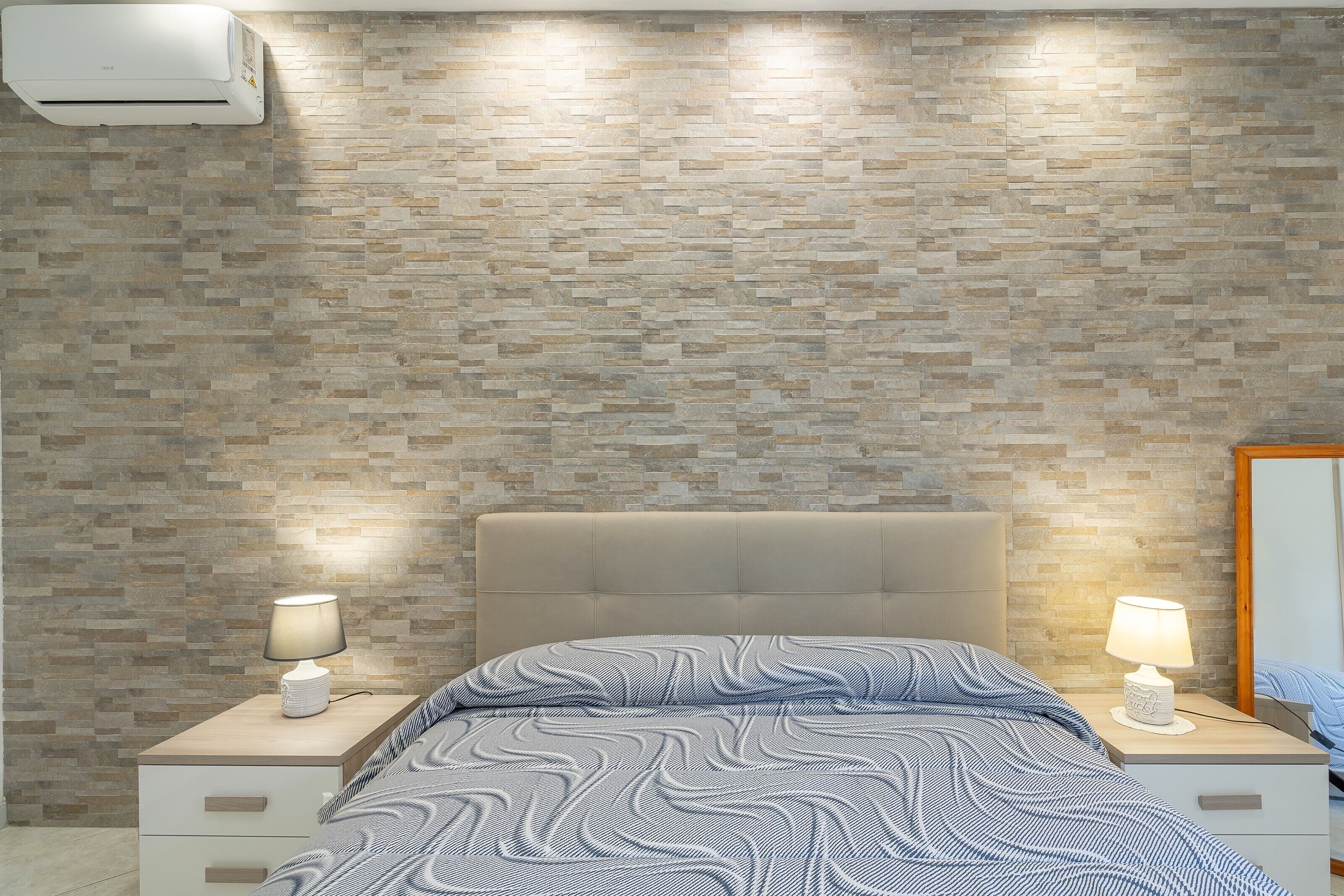 A bedroom with a patterned wall, a bed with a headboard, bedside tables with lamps, and a wardrobe.