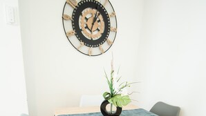 A dining area with a wooden table, two chairs, a clock, and a plant on the table.