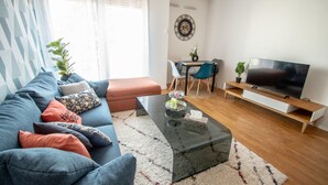 A modern living room with a sofa, coffee table, TV, and a dining area with chairs and a table.