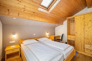 Une chambre avec deux lits, un plafond en bois, une lucarne, une armoire et une chaise.