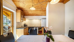 Un comedor con una mesa, sillas, un jarrón con flores, una cocina al fondo y vigas de madera en el techo.