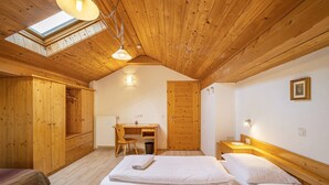 Una habitación con techos de madera, tragaluces, un escritorio con silla y tres camas.