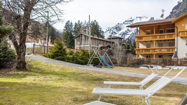 Un hotel con terraza exterior, parque infantil y montañas al fondo.