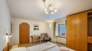 Un dormitorio con dos camas, un armario de madera, un escritorio con silla y una ventana con cortinas.