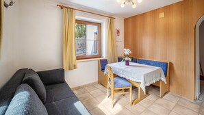 Une pièce comprenant un canapé, une table avec des chaises, une fenêtre avec des rideaux, un mur en bois et un luminaire au plafond.