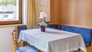Une pièce avec une table recouverte d’une nappe en dentelle blanche, un vase violet contenant des fleurs blanches et des sièges rembourrés de tissu bleu.