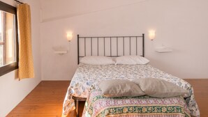 Ein Einzelbett mit einem gemusterten Überwurf, zwei Wandleuchten und ein Fenster mit Vorhang.