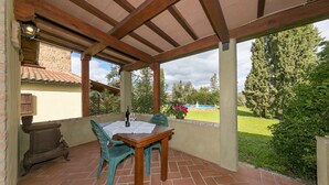 A covered patio with a wooden table and chairs, a brick floor, and a view of a garden. - Agriturismo "Il Nazareno - Il Coppaio" with Shared Pool and Wi-Fi (cecina)
