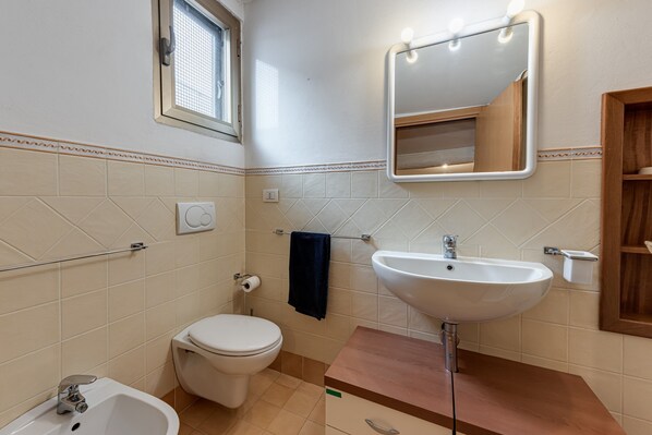 Une salle de bain équipée de toilettes, d’un lavabo, d’un miroir et d’une fenêtre.